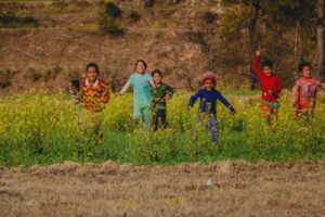A group of cheerful children playing in a mustard flower field in rural India on a sunny day.